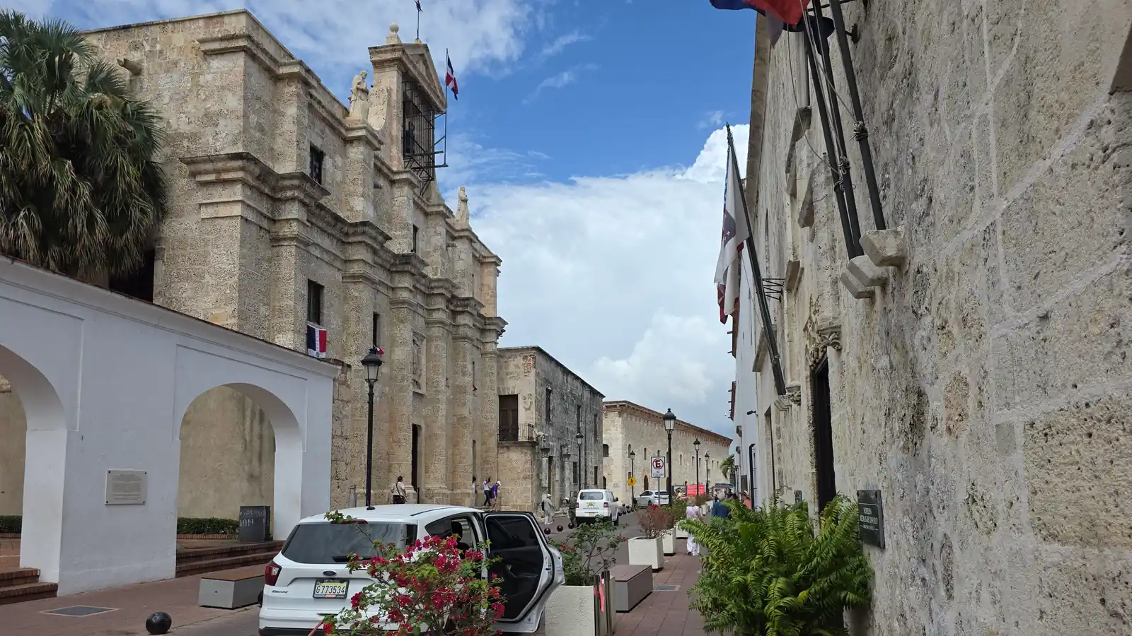 La calle Las Damas en la Zona Colonial de Santo Domingo, entre fachadas de piedra caliza del siglo XVI, con la bandera dominicana ondeando sobre un edificio.