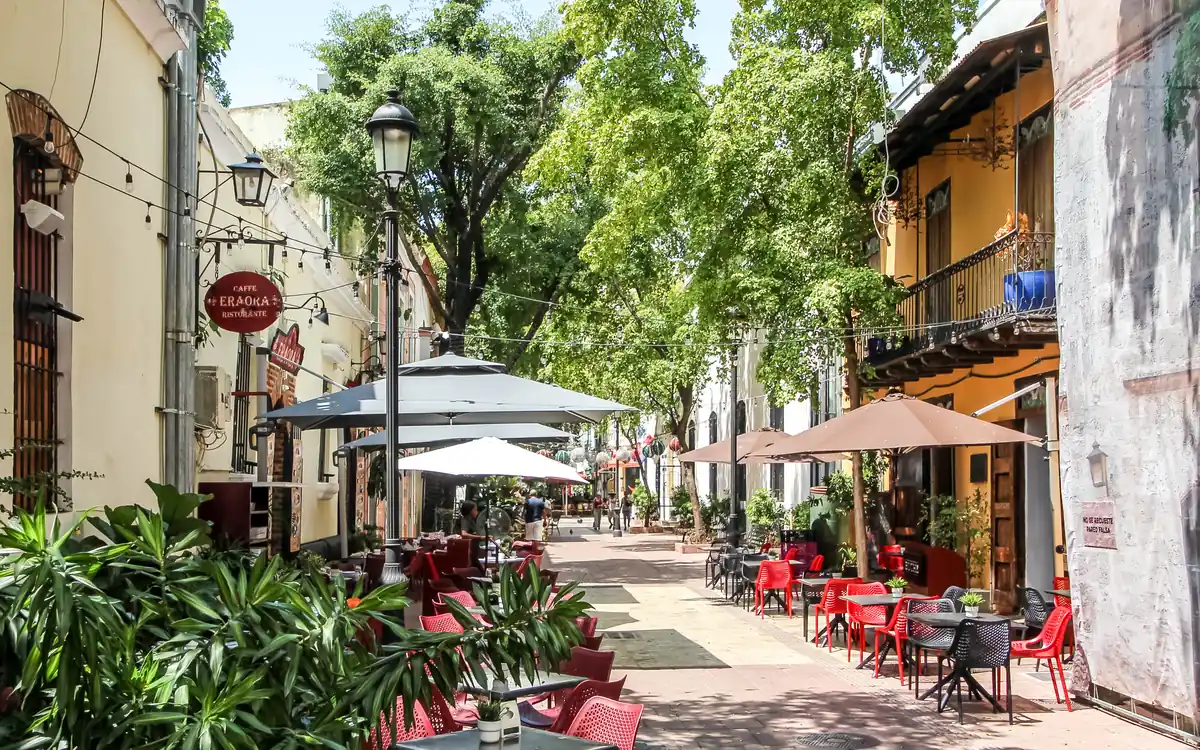 Terraza de restaurante con sombrillas y sillas rojas en la calle El Conde, una vía peatonal arbolada de la Zona Colonial de Santo Domingo.
