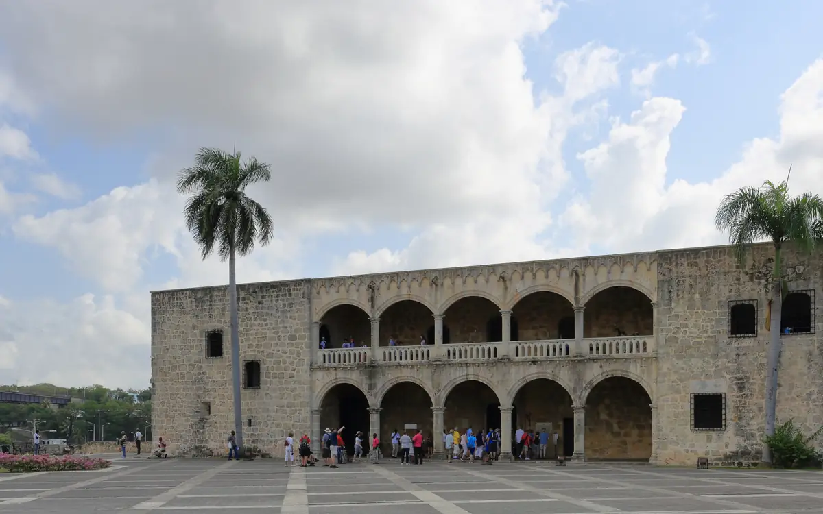 Fachada de piedra del Alcázar de Colón en Santo Domingo, con dos niveles de arcadas sobre una explanada empedrada.